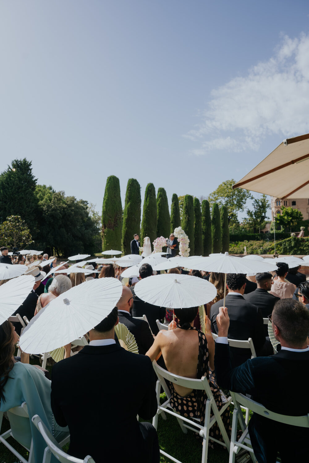 Guests holding white parasols during the outdoor Jewish wedding ceremony at Castell de Sant Marçal
