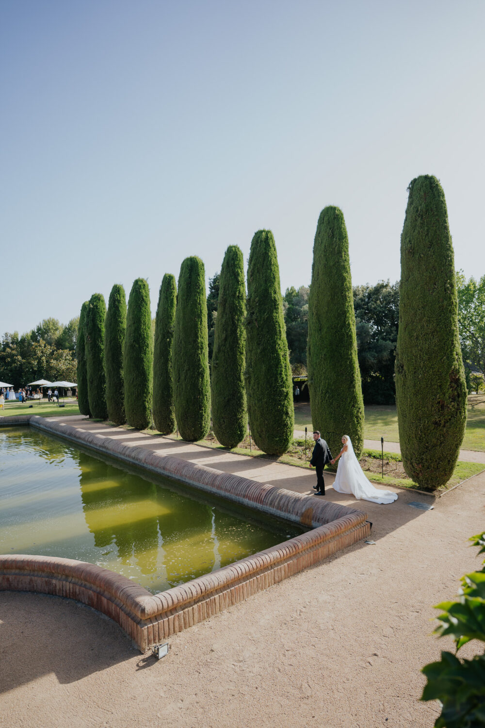 Reception tables set with white linens and florals under the trees at Castell de Sant Marçal