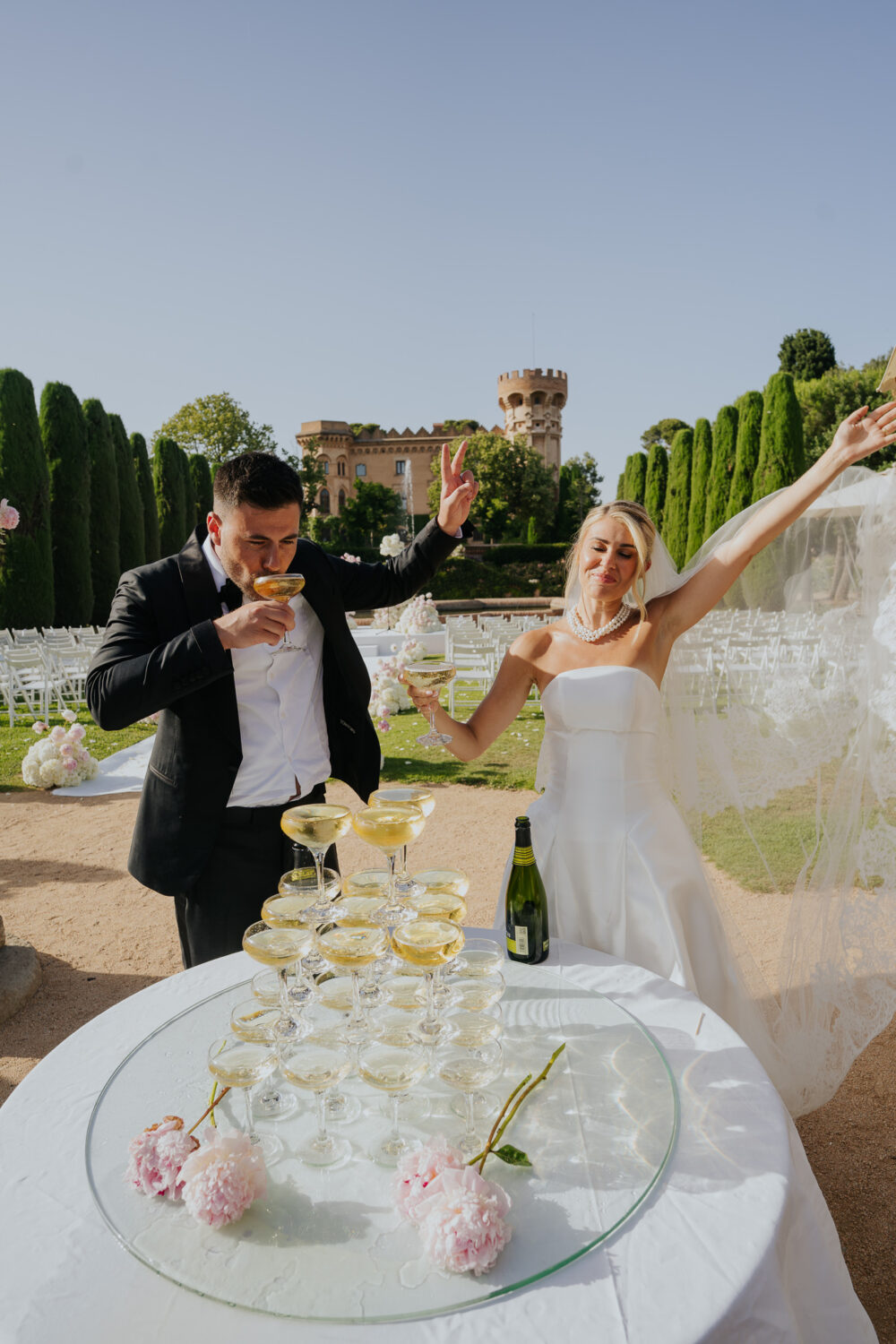 Bride and groom laughing together beside the fountain and cypress trees at Castell de Sant Marçal