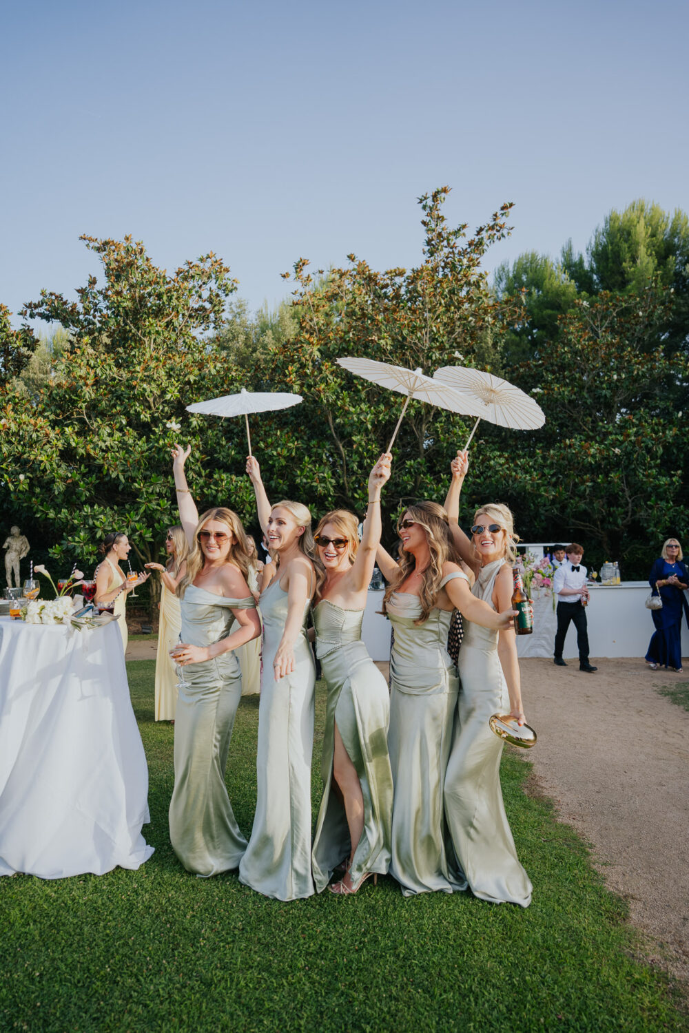 Bridesmaids celebrating with parasols and drinks on the lawn after the ceremony