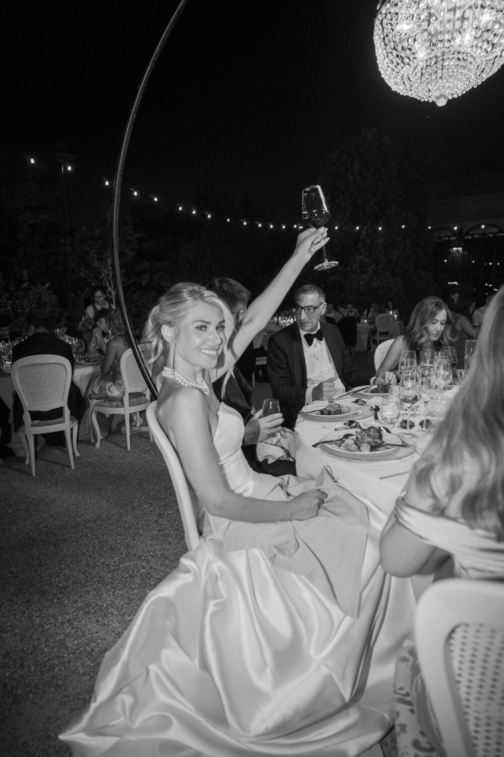 Black and white photo of the bride raising her glass in a toast during the reception dinner